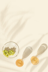Wine glasses with white wine and green grape on beige background palm leaf shadow at sunlight. Summer alcohol drinks concept, colored glassware. Top view minimal aesthetic still life photo
