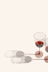 Minimal summer still life with glasses of red wine, sunlight shadow on beige background, copy...