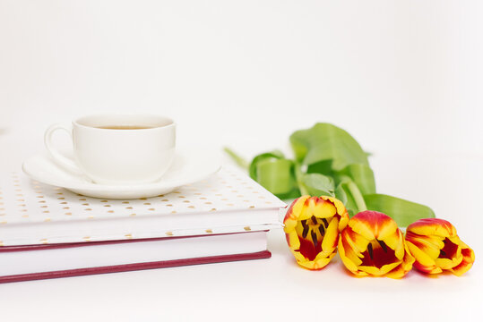 Spring greeting card. Notebooks, a bouquet of tulips and a cup of tea on a white background