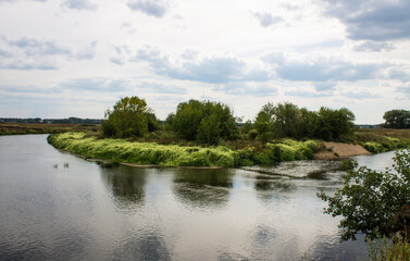 Beautiful landscape - the Klyazma river between the banks with green grass and trees against a cloudy sky on a summer day in the Moscow region and copy space