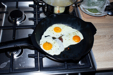 cooking breakfast at home. dirty stove. scrambled eggs in a pan. fried eggs with spices.