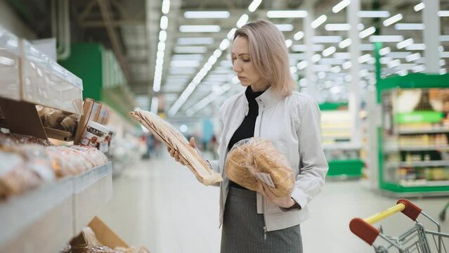 A woman in a large supermarket buys fresh bread. Large selection of rolls and loaves on the shelves of the bread department