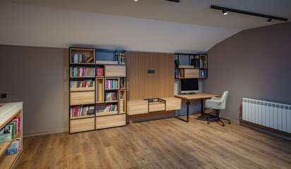 Workspace with computer and shelves with books. Comfortable office chair near table with modern computer. Stylish home office interior with comfortable workplace and wooden floor.