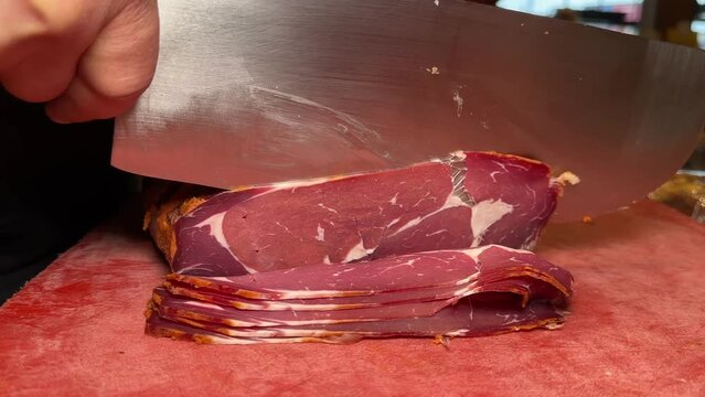 Close-up of cutting turkish pastrami on board. Attendant slicing pastrami at the deli counter