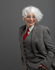 Smiling mature businesswoman in glasses and suit standing with hands in pockets