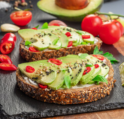 Avocado toasts - bread with avocado slices, pieces of red pepper and sesame  on black stone board.