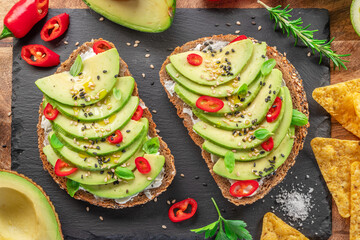 Avocado toasts - bread with avocado slices, pieces of red pepper and sesame on black stone board.