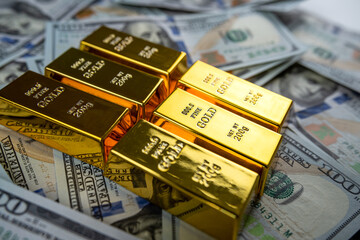 closeup gold bar lying on 100 dollar bills