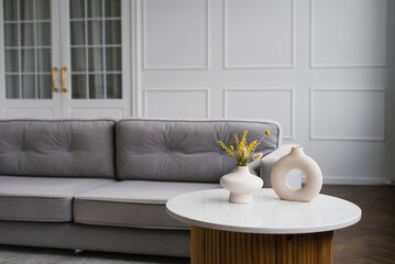 Modern stylish vases on the coffee table near the gray sofa in the living room of the house