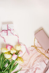 Women's clothing, gift box, bag and tulip flowers. Minimalistic composition in pastel beige and pink tones. Top view, flat layout, copy space. The concept of a woman's birthday, fashion and blogging