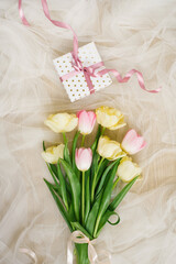 A beautiful spring bouquet of pink and yellow tulips and a gift with a ribbon on a beige background. Flat lay and copy space