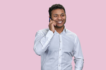 Positive indian businessman is having a phone conversation. Brown man in white shirt talking on phone. Isolated on pink background.