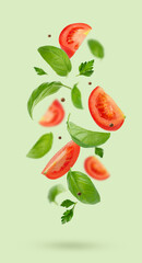 Flying tomatoes, parsley and basil leaves on green background. Vertical composition