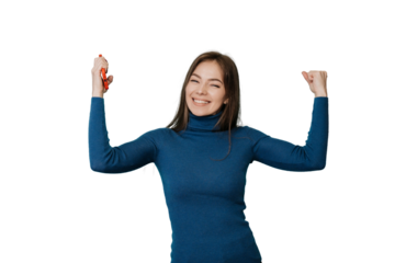 Celebrating young attractive girl raises her hands up smiling holding phone, happy received good news, standing over transparent background. Happy Italian young woman clenched her hands like a winner.