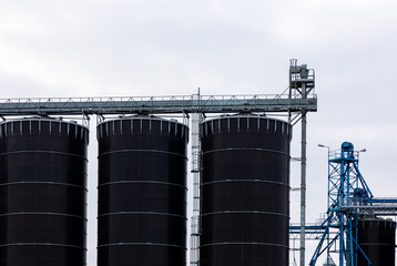 Obraz premium A huge, blackm steel grain silo standing in a field. Warehouses full of grain before the new season