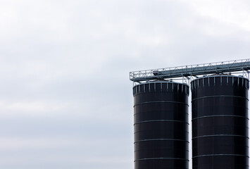 A huge, blackm steel grain silo standing in a field. Warehouses full of grain before the new season