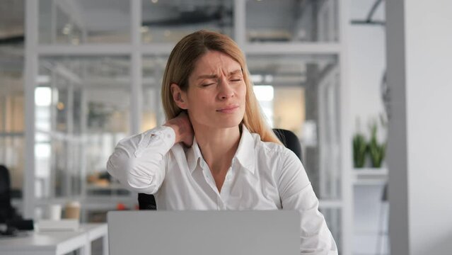 Tired businesswoman is experiencing neck pain while working in office. Female holding her neck with her hand. Business lady having busy workday. Exhausted professional suffering from Neck Pain.