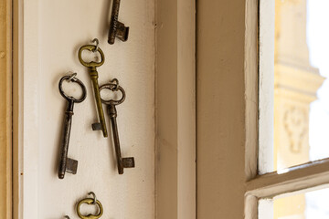 A collection of old steel keys for historical locks. The keys hang on a wooden window frame.