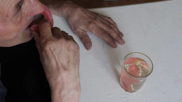 the pensioner takes out dentures from a glass of water and puts them on. removable dentures, dental prosthetics. elderly people concept.be healthy concept
