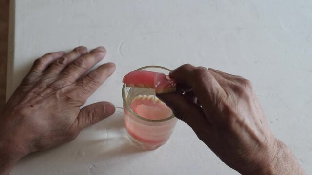 an elderly man takes out dentures from a glass of water and puts them on in his mouth. loss of teeth, dental prosthetics. elderly people concept.be healthy concept
