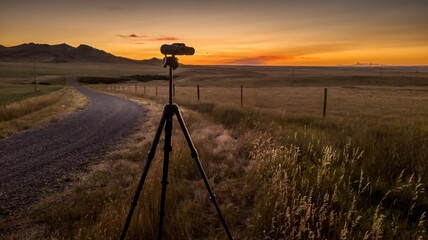 Tripod with a camera in the field a dusty path near and purple sky in the background