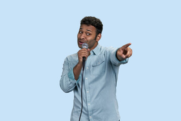 Portrait of an indian singer pointing at someone from audience. Isolated on pale blue background.
