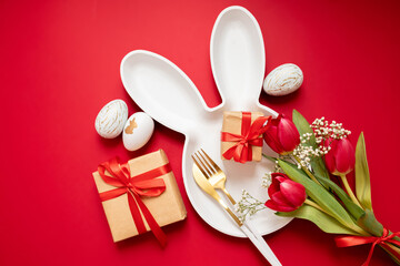easter eggs, flowers, gifts and bunny plate with cutlery on a red bright background. easter frame layout. place for text. woopy space. flat lay. top view.