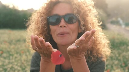 Woman blowing poppy petals flower in spring celebration season outdoors leisure activity. One pretty adult female people enjoy summer. Portrait of young lady with curly hair and sunglasses having fun