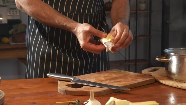A man cleans and cuts raw smoked sausage on a cutting board against the backdrop of a kitchen interior. Culinary footage. Blogger hosts a cooking show