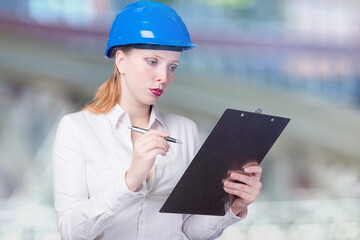 Young female engineer wearing a blue hard hat is working with a note pad