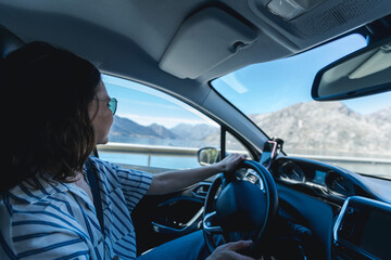 Young pretty cheerful woman in sunglasses driving a car along sea coast in the mountains