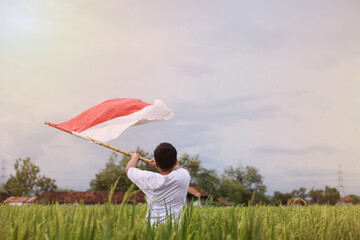 Back view of Asian boy celebrate Indonesia Independence Day on 17 August by hoisting a flag