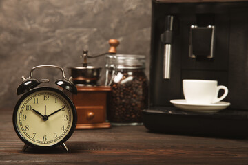 Alarm clock and a cup of morning coffee with a coffee machine on the background of the kitchen...