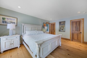 Interior shot of a bedroom with a bed with white sheets, light green walls and wooden floor.