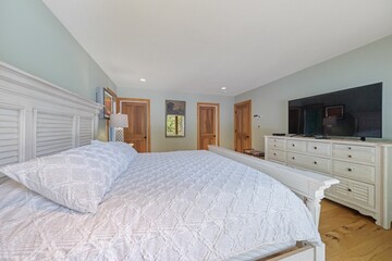 Interior shot of a bedroom with a bed with white sheets, light green walls and a TV.