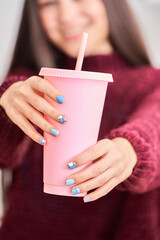 Obraz na płótnie Canvas Woman holding a pink plastic cup while showing her manicure nails. Manicure and beauty concept.