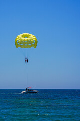 Parasailing on a yellow parachute against the blue sky. Beach extreme adventures. Background vacation, photo for postcards, tourist and travel guide. The concept of summer holidays, vacation, tourism