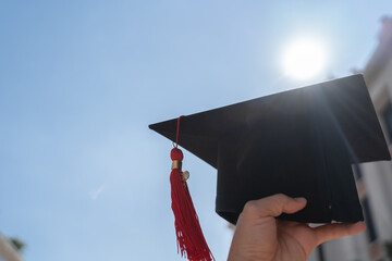 Graduation day concept, Graduation cap was holding on the air with blue sky background. Graduation hat is mean graduate from education or learning, knowledge, studying and congratulation on education. - 588291763