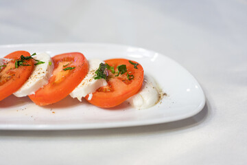 Italian Caprese Salad with Mozzarella cheese, tomatoes, basil, olive oil on white plate at Italian diner, restaurant. Fresh Caprese is traditional Italian food from Italy. Traditional food concept.