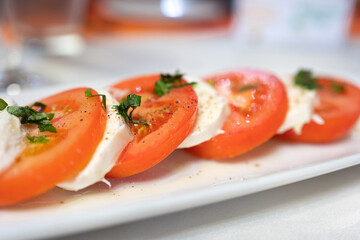 Italian Caprese Salad with Mozzarella cheese, tomatoes, basil, olive oil on white plate at Italian diner, restaurant. Fresh Caprese is traditional Italian food from Italy. Traditional food concept.