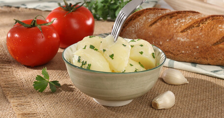 boiled potatoes in a bowl. farm products on the table. simple country food. potato dish with tomatoes and bread on burlap. natural food on a sunny day.