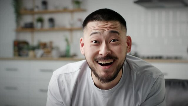 Exited Asian Man showing Wow Emotion at Camera. 30s male laughing starring at camera sitting on couch at home.