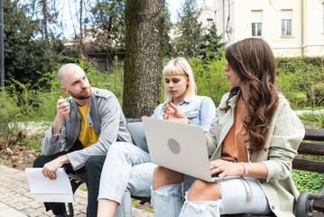 Young business people are sitting in the park on a bench having a staff meeting looking for premises or an apartment for rent to move their small company into an office. Young enthusiastic experts