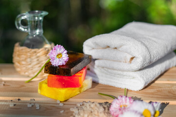 Obraz na płótnie Canvas Towels, soap, bath salts and daisies for natural spa treatments on a wooden table against the greenery of the garden.
