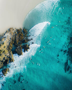 Aerial view of people with a surfboard along the coastline in Byron Bay, New South Wales, Australia.