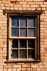 Closeup of a window with a wooden frame and an old red brick wall with damaged texture