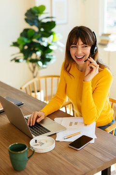 Happy freelancer listening through headset at home office