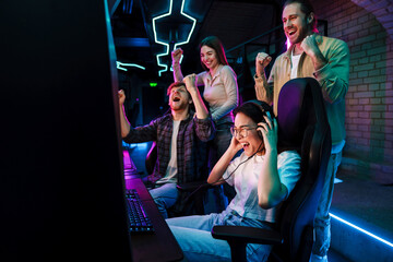 Group of friends celebrating victory of asian girl in video game while standing next to her in cybersport club © Drobot Dean