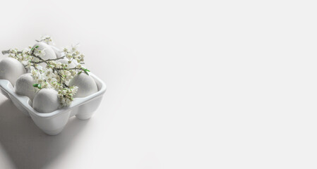 White eggs in egg container with cherry blossom at white background. Easter concept