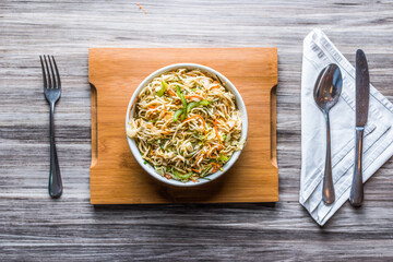 Hakka Noodles Vegetables with spoon and tissue isolated on wooden board top view on table fastfood